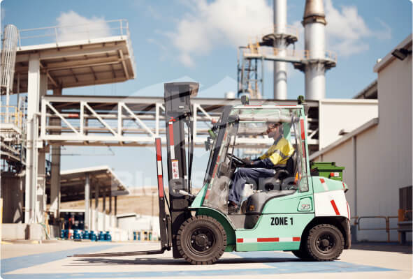 Man driving forklift truck outside across a manufacturing facility 